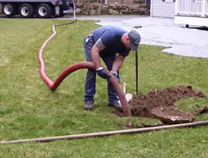 Septic pumping technician servicing a residential septic tank with a vacuum hose in Bloomington, IN