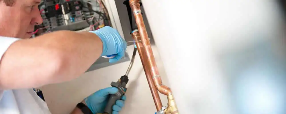 Water heater repair technician testing copper pipe connections and controls in Bloomington, IN